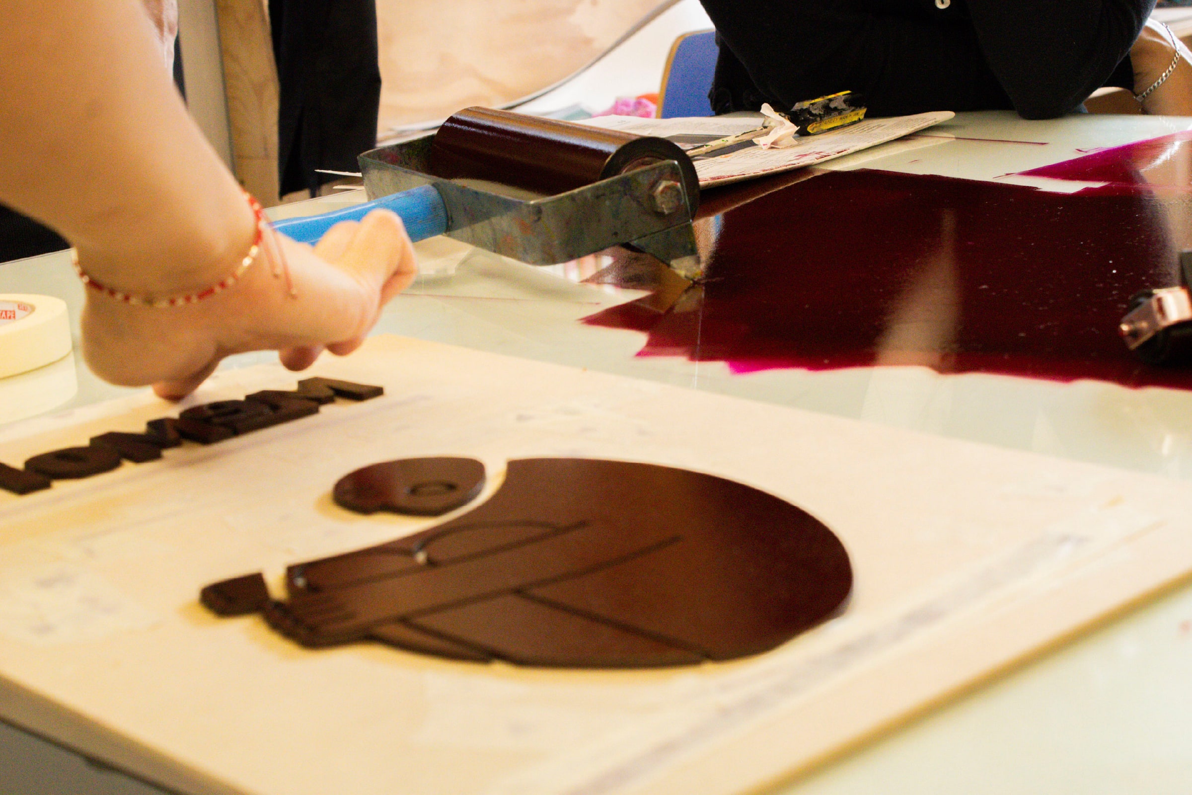 Dos manos extienden tinta roja oscura sobre la matriz de corte láser con una espátula.