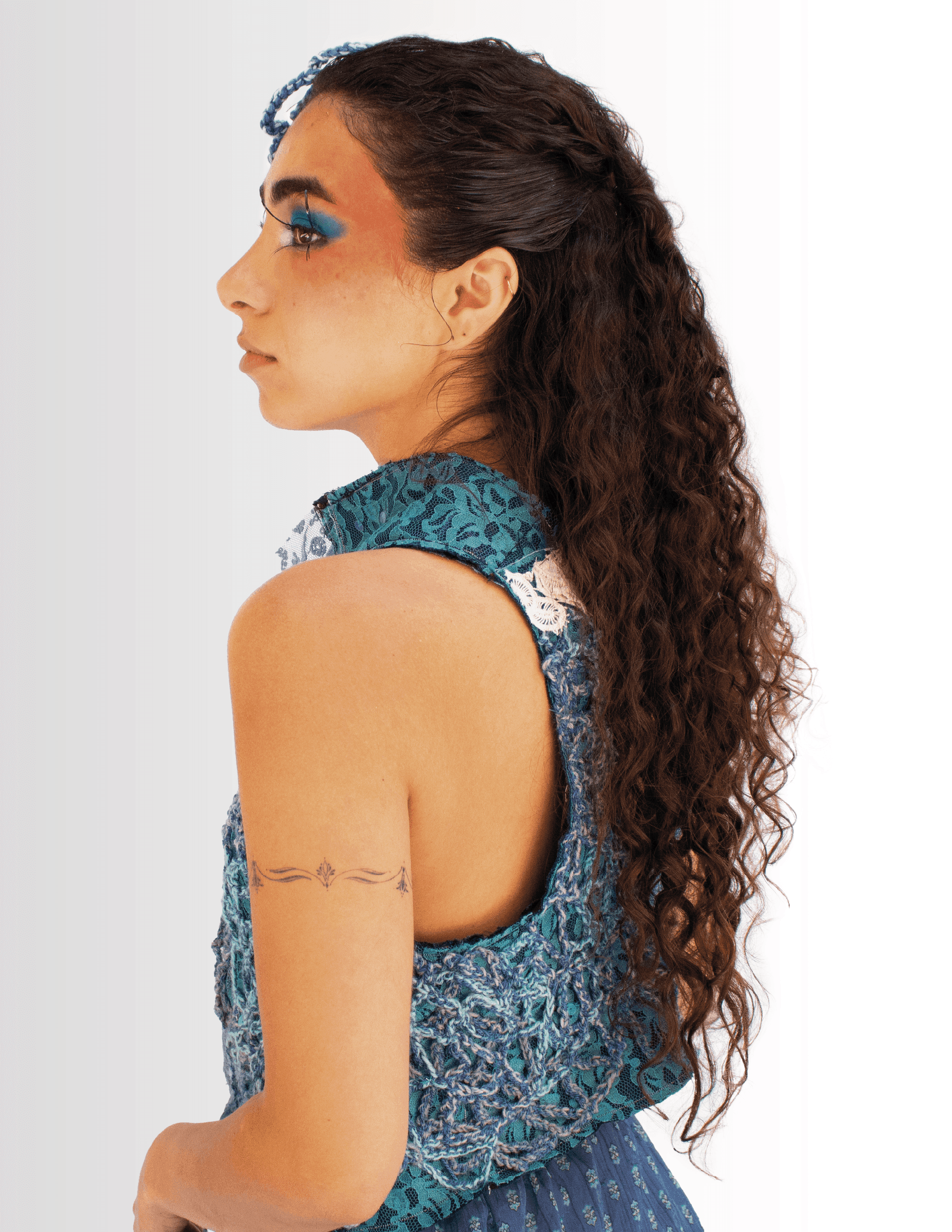 Retrato de perfil de una modelo con delineado azul, con un top de crochet turquesa.