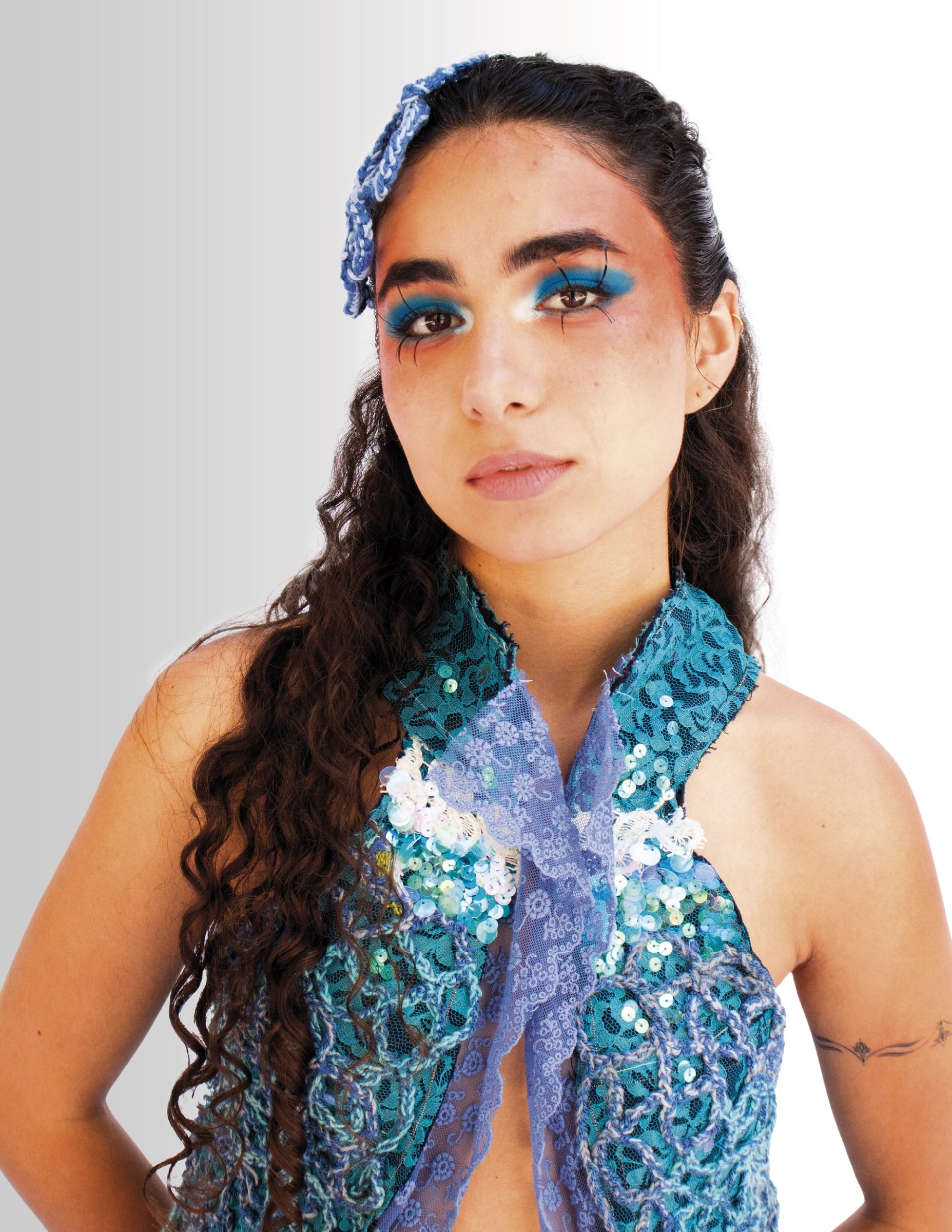 Retrato de la modelo con delineado azul, tocado de crochet y un chal turquesa.