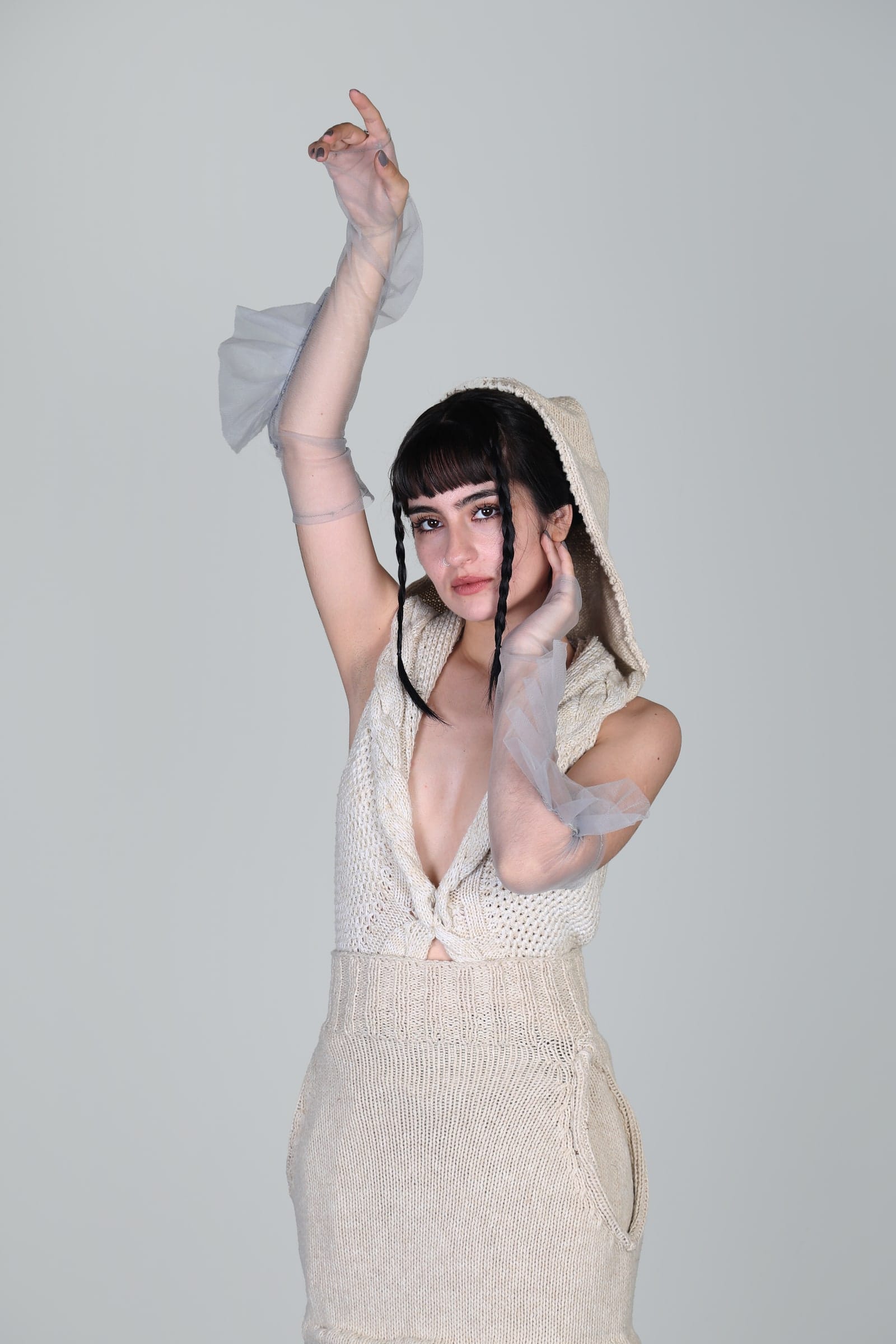 Modelo en estudio con un vestido de punto crudo, los brazos levantados sobre la cabeza.