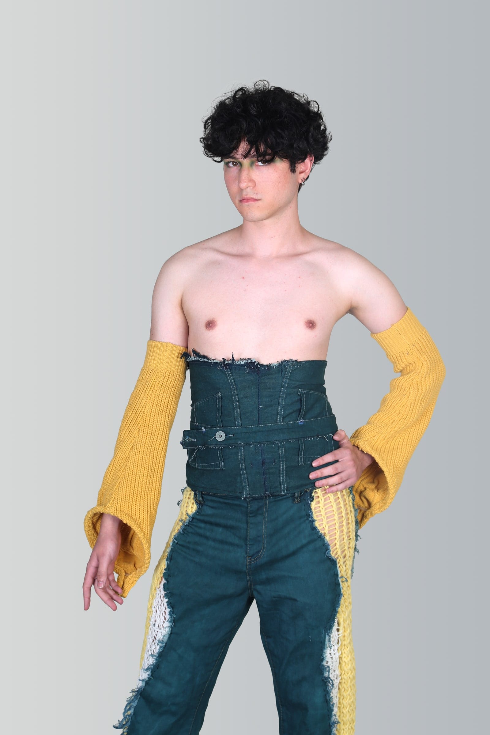 Modelo en estudio con un corsé de denim verde y mangas de punto amarillo.